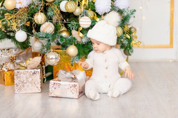 宝宝在圣诞树旁拿着礼物的新年照片图片下载