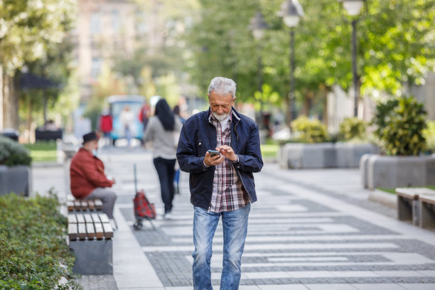 一位老人走在市区里，边走边讲手机。图片下载