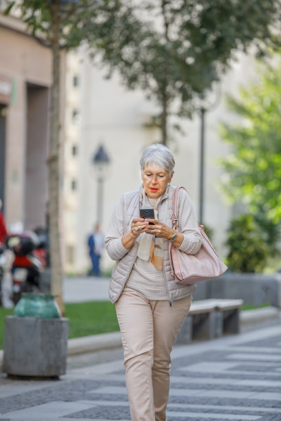 带着手机的高级女士正前往城市街道上班。图片下载