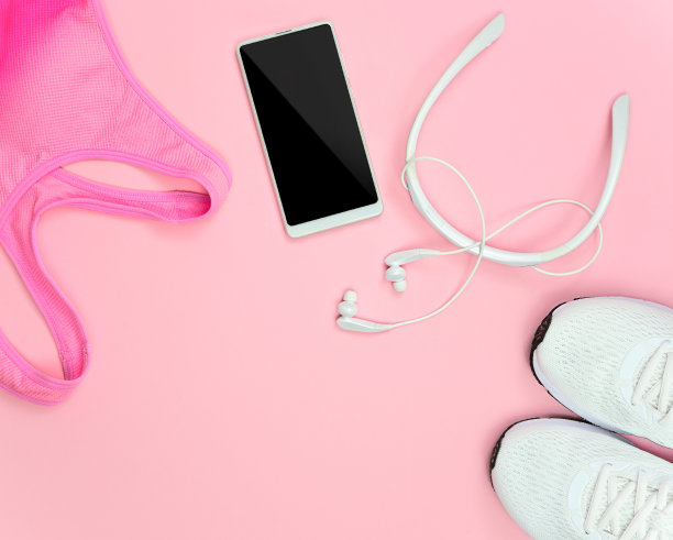 一双白色运动鞋，耳机，运动胸罩，粉色背景上的手机。图片下载