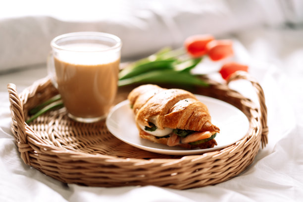 白色的床上放着牛角面包和咖啡，柳条托盘上放着鲜花图片下载