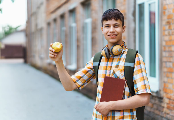 快乐少年的肖像在上学的路上，他正在吃苹果，教育和回学校的概念图片下载