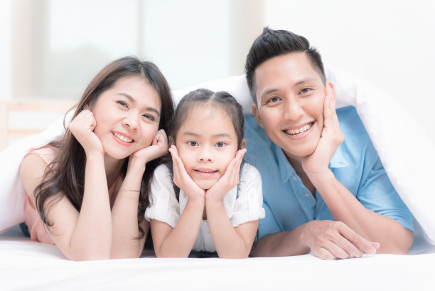 幸福的家在卧室的白色床上。妈妈、爸爸和孩子们在家里的床上玩耍。三口之家好健康。图片下载