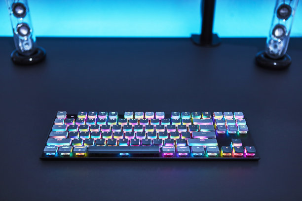 灰色书桌上的彩色背光游戏机键盘。蓝色发光的墙。图片下载