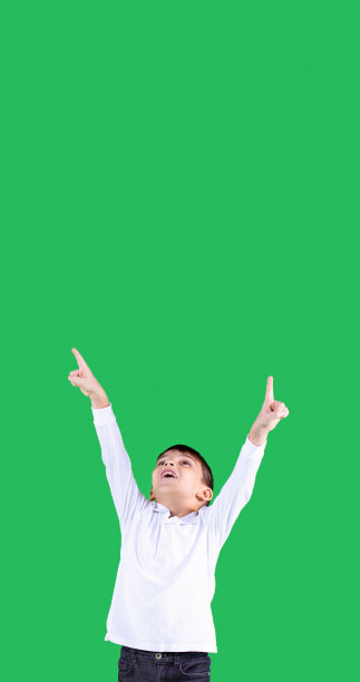 一个穿着白色t恤的快乐男孩微笑着站在那里，举起双手看着并指着空中的什么东西。图片下载