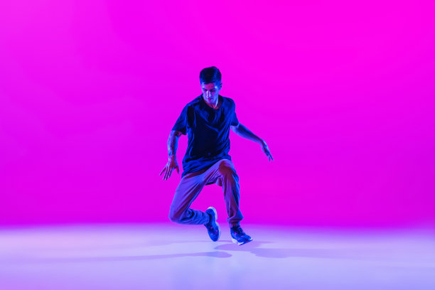 在霓虹灯下的舞厅里，年轻时髦的嘻哈舞者身着现代服装，在明亮的紫红色背景下跳着独舞。图片下载