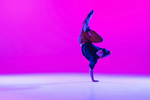 在霓虹灯下的舞厅里，一个跳舞的男子，霹雳舞者，穿着现代服装，在明亮的洋红色背景下孤立地运动。图片下载