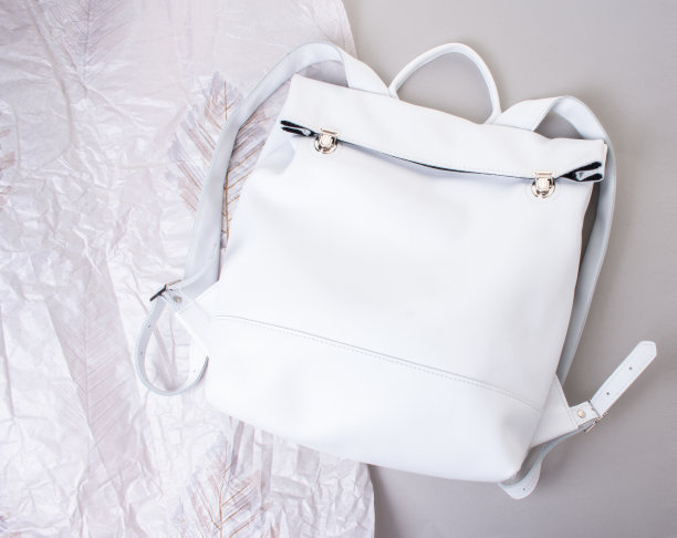 白色手工皮革背包在灰色背景和皱巴巴的纸图片下载