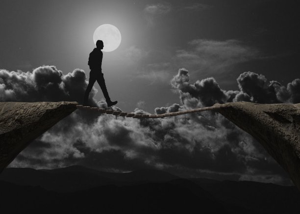 一个男人的剪影在一个黑暗的夜晚通过一座小桥的悬崖图片下载