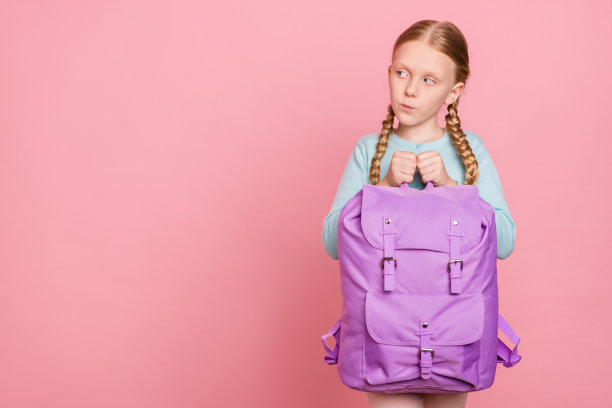 照片中的漂亮女生身穿蓝色开襟羊毛衫，手持帆布背包，看上去空荡荡的，孤立的粉红色背景图片下载