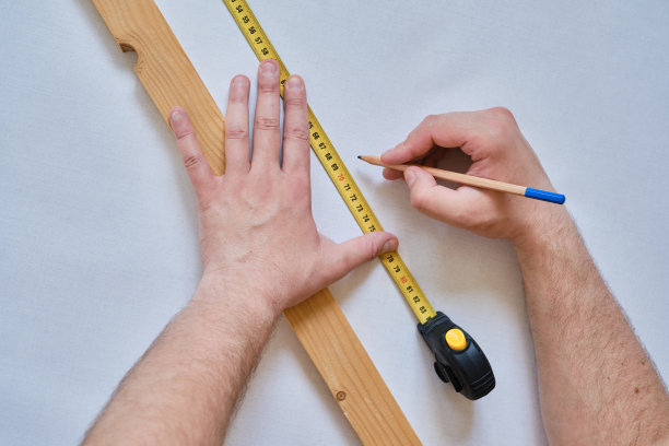 一个人用卷尺量一块木头。工人进行修理。建筑工，修理工做铅笔记号。建设、改造工作图片下载