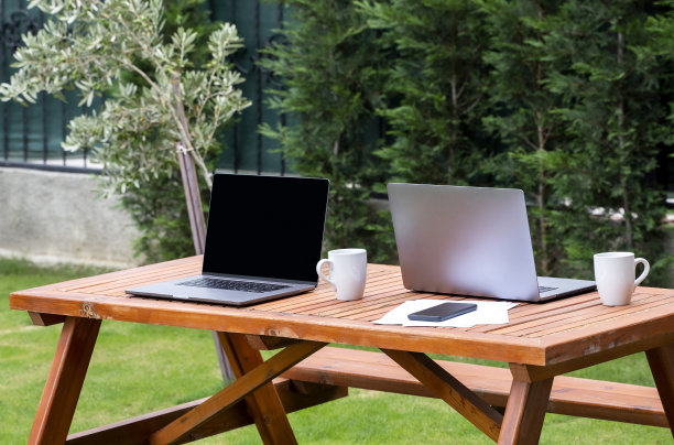 两台现代笔记本电脑放在后院的木桌上，在家工作的概念图片下载