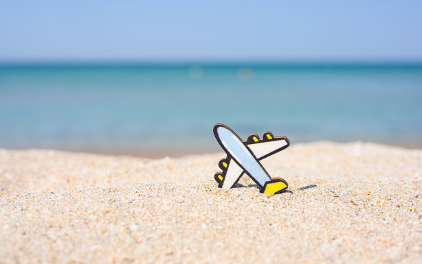 在蓝色大海的映衬下，一架小的木制玩具飞机躺在沙滩上图片下载