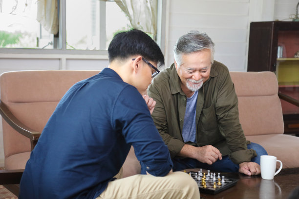 亚洲老人和儿子在客厅下棋，为长辈和家庭概念图片下载