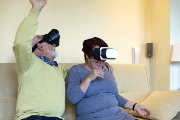 家中客厅里的老夫妇正戴着虚拟现实眼镜，用手做着手势。图片下载