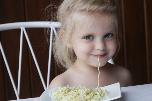 蹒跚学步的小女孩在吃面条或意大利面。图片下载