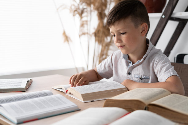 神童坐在图书馆的桌子前打开书本或课本看书。学生做家庭作业的知识来自文学。概念返校图片下载
