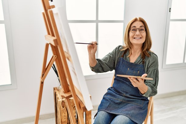 中年艺术家妇女微笑着在画室快乐绘画。图片下载