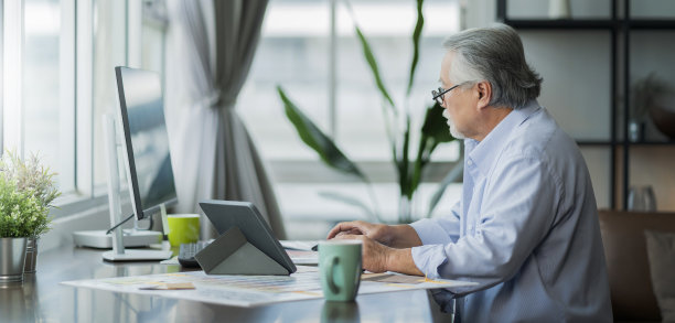 老亚洲高级退休年龄在家里工作手ise桌面和文件文件在客厅家的内部背景，亚洲男性高级工作在家里图片下载