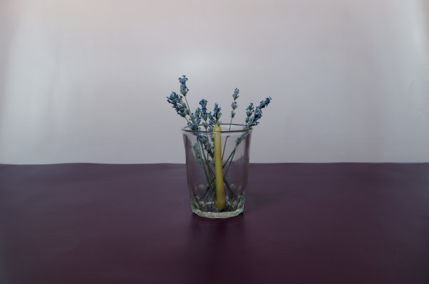 带干薰衣草花的细枝和教堂蜡烛，在一个透明的玻璃在一个普通的背景图片下载