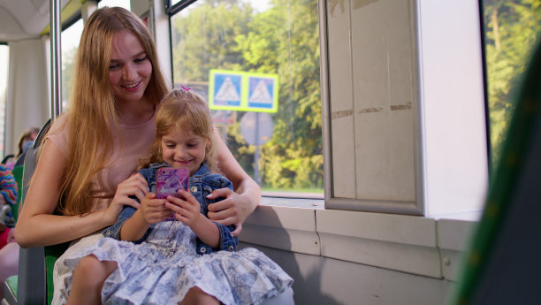 母亲带着女儿乘车回家，玩智能手机，浏览社交媒体图片下载