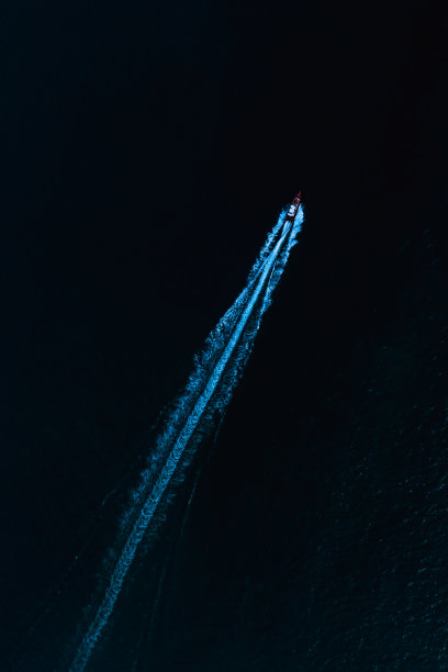 快艇在暗夜碧蓝的海面上用溅起的水花驾驶着船夫俯视图图片下载