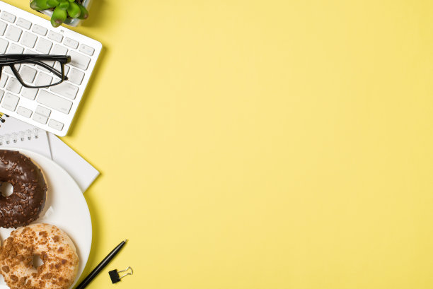 顶视图照片的工作场所眼镜键盘植物提醒夹笔和盘甜甜圈孤立的淡黄色背景与空白图片下载