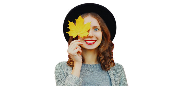 秋日幸福微笑的年轻女子肖像，用黄色的枫叶盖住眼睛，头戴黑色圆帽，灰色针织毛衣孤立在白色背景上图片下载