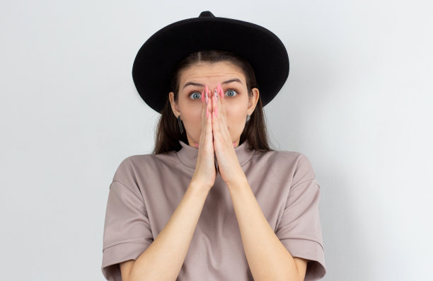 年轻漂亮的女人感到担心，不安和害怕，用手捂住嘴，看起来焦虑，在白色的墙壁上搞砸了图片下载