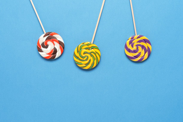 蓝色蜡笔纸背景上的彩色棒棒糖。俯视图，平铺，复制空间。明亮喜庆的背景。图片下载