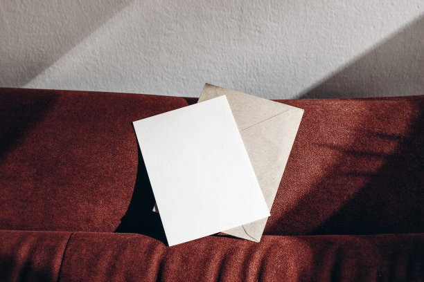 空白的贺卡模型，信封在阳光下生锈的天鹅绒沙发上。空洞的请柬越过白色的墙和阴影。细节优雅的室内，室内空间。现代品牌的概念。有选择性的重点。图片下载