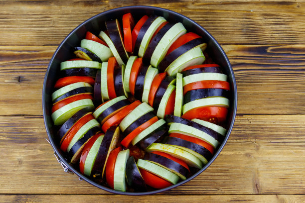 炖菜的准备。木制桌子上圆形烤盘里的杂烩蔬菜。法国传统蔬菜图片下载