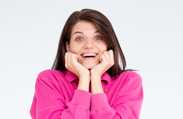 近距离拍摄的漂亮可爱的女孩，蓝色的眼睛和纯净的皮肤微笑着，露出她洁白均匀的牙齿，下巴下牵着手，有令人愉快的表情图片下载