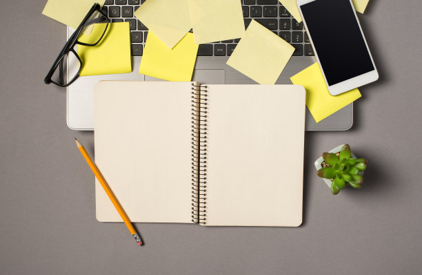 顶部视图照片黄色便利贴眼镜智能手机在笔记本电脑键盘植物和铅笔在打开的螺旋记事本上孤立的灰色背景与空白图片下载