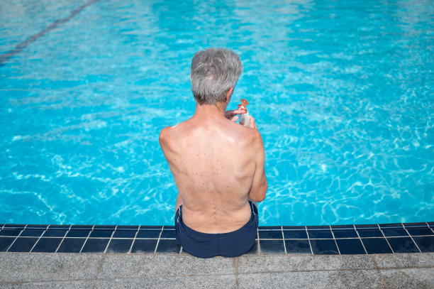 老年男人在游泳池边休息和晒日光浴时涂抹防晒霜以保护皮肤图片下载