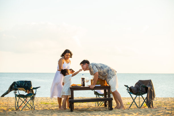 幸福的亚洲家庭，一对父母带着小女儿在沙滩上享受晚餐聚会在夏天的日落。图片下载