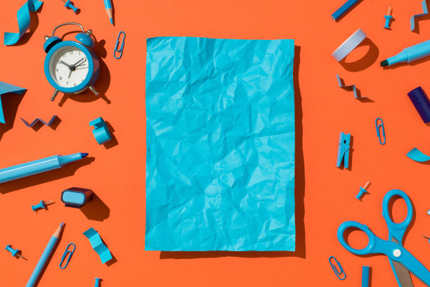 顶视图照片生动的蓝色皱巴巴的纸页和学校配件蓝色文具孤立的橙色背景与copyspace图片下载