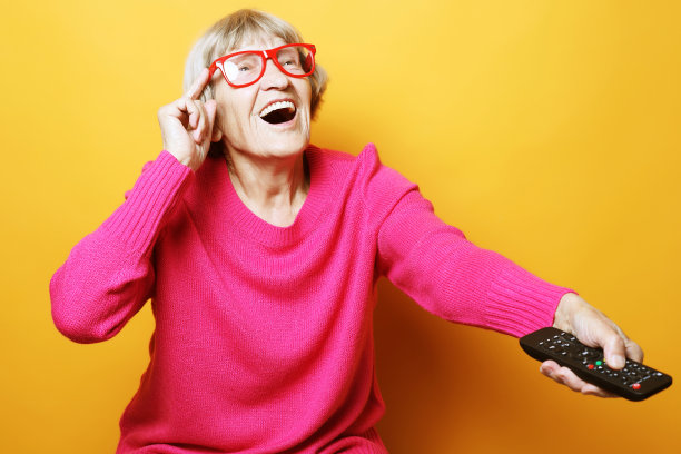 生活方式和人物观念:搞笑的祖母拿着电视遥控器，背景是黄色的图片下载