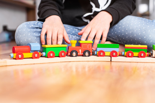 可爱的小女孩玩木制火车玩具。木制火车玩具。可爱的小女孩玩木制火车，建造玩具铁路。可爱的女孩玩起重机和汽车。学龄前儿童教育玩具。图片下载