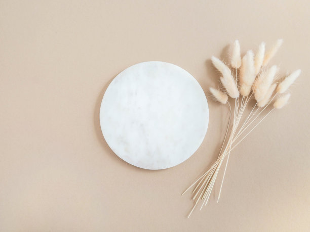 大理石白色圆形讲台和干拉古鲁花束米色背景。图片下载