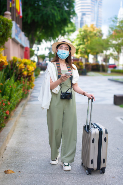 年轻的亚洲游客戴着防护口罩，提着行李箱在市中心行走图片下载