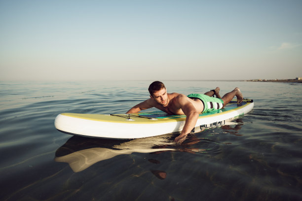 年轻健康的男子在桨板上漂浮在湖面上。图片下载