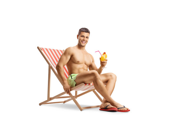 穿着游泳短裤的健美男子坐在沙滩椅上，手里拿着一杯鸡尾酒图片下载