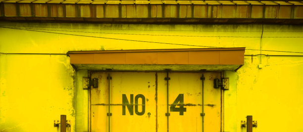 旧工厂黄色仓库，屋顶褪色，4号门生锈图片下载