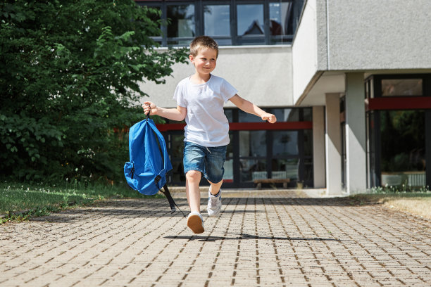 快乐的男孩在放学后背着书包从学校跑出来。假期的开始。图片下载