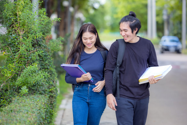 一对年轻的大学生在去上课的路上。他们一边读书一边在校园里散步。秋天是一个美丽的季节。图片下载