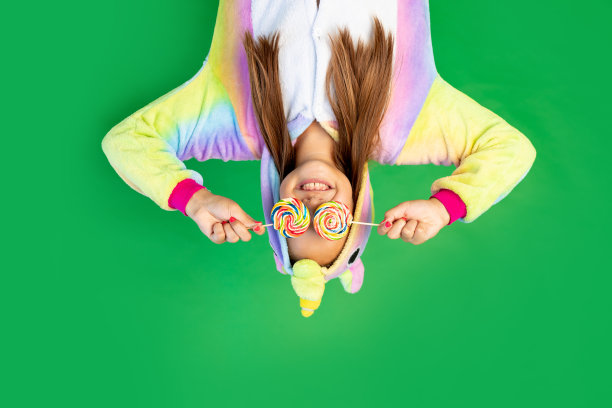 可爱的小女孩们穿着红色的独角兽服装，在一个绿色的孤立背景下，眼睛上戴着大棒棒糖。空间的文本。节日的概念图片下载