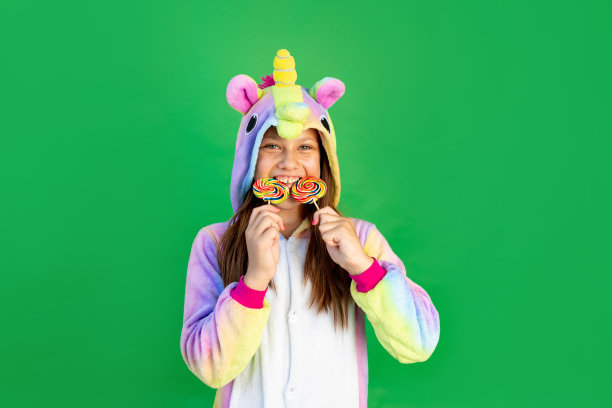 可爱的小女孩们穿着红色的独角兽服装，在一个绿色的孤立背景下，眼睛上戴着大棒棒糖。空间的文本。节日的概念图片下载