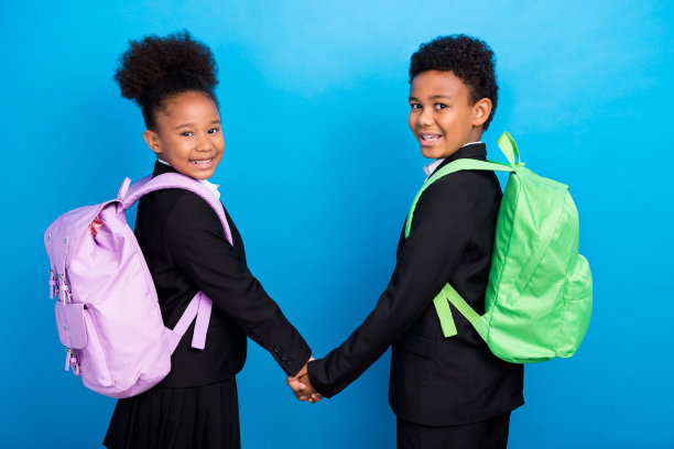 转照片的快乐积极开朗的非洲裔美国儿童手牵手，穿背包孤立在蓝色背景图片下载