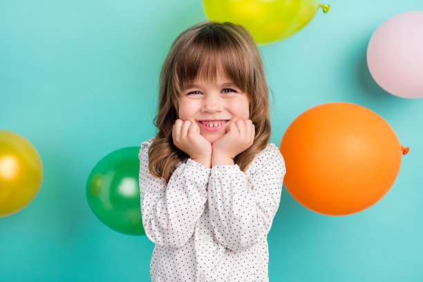 照片中的小甜甜女孩双手捂脸，身穿白色衬衫，孤立在蓝色背景上图片下载